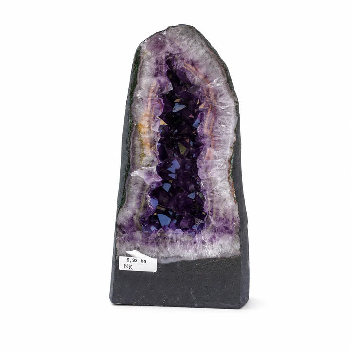 Natūrali ametisto geoda su ryškiai violetiniais kristalais baltame fone.